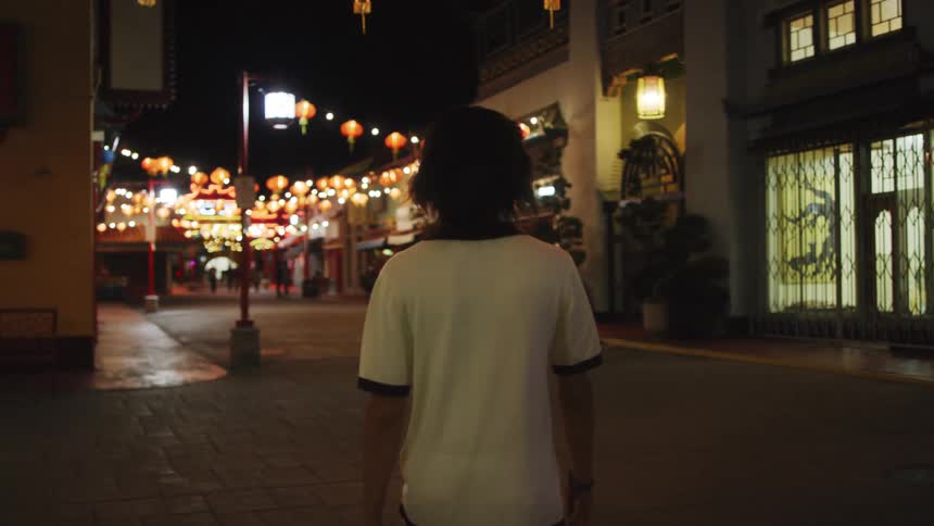 Person in white t-shirt walking in Asian suburb at night
