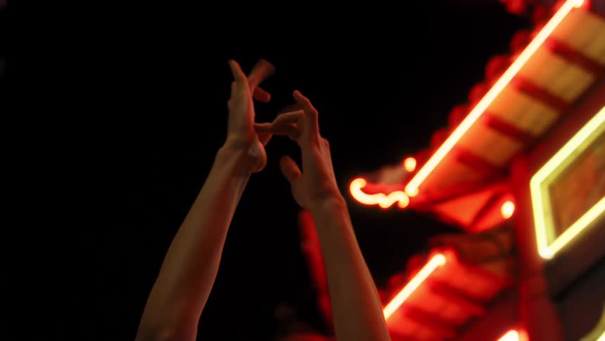 Hands perform movements and gestures near an asian style building decorated with lights