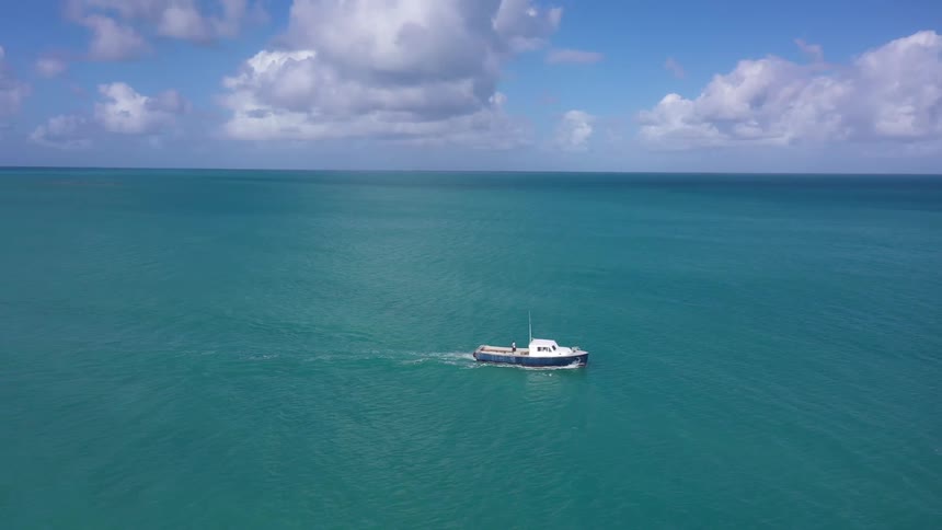 People walk around in the back of a yacht moving across the ocean on a cloudy day