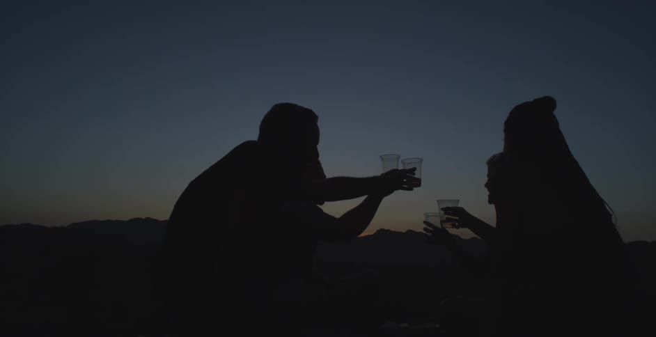 Silhouette of four people toasting and drinking while standing in an outdoor setting in the mountains at dusk