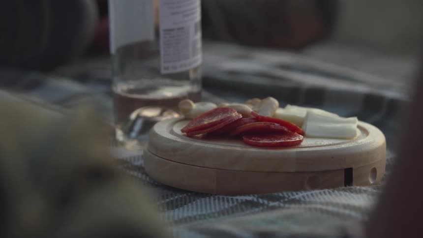 People sitting around a bottle of wine and salami in an outdoor setting