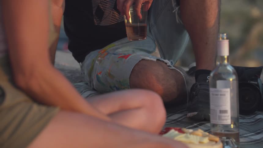 Bottle of wine next to a camera in the middle of three people outdoors
