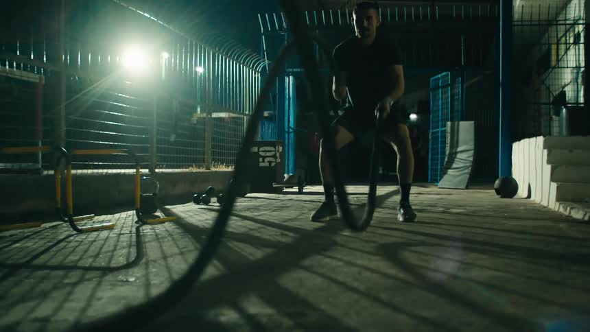 Man in a gym at night in an outdoor setting hitting ropes