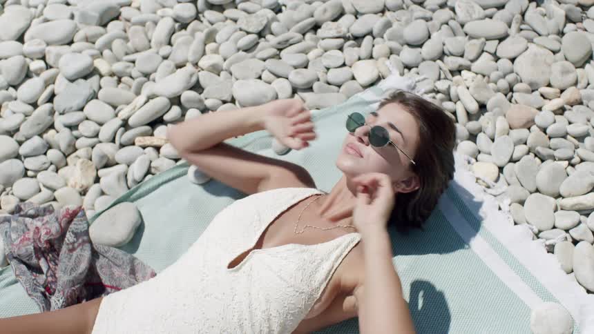 Woman in swimsuit and sunglasses lying on towel