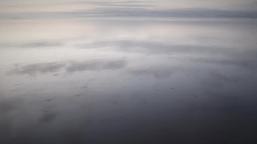 A calm misty expanse of water mirrors the overcast sky in a tranquil minimalist scene