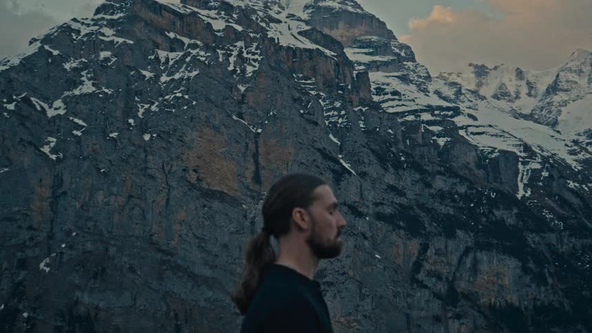 Close up portrait of a young man standing outdoors contemplatively in front of a mountain outdoors during daytime