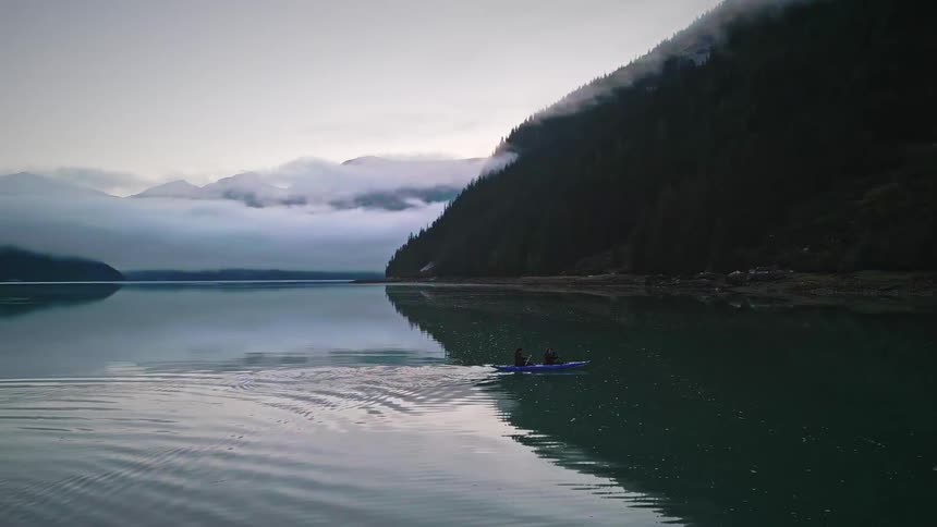 Two people canoeing on a calm lake surrounded by mountains