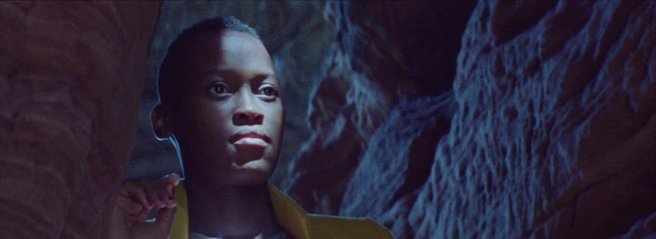 A young woman is standing inside a cave with light reflecting on her face