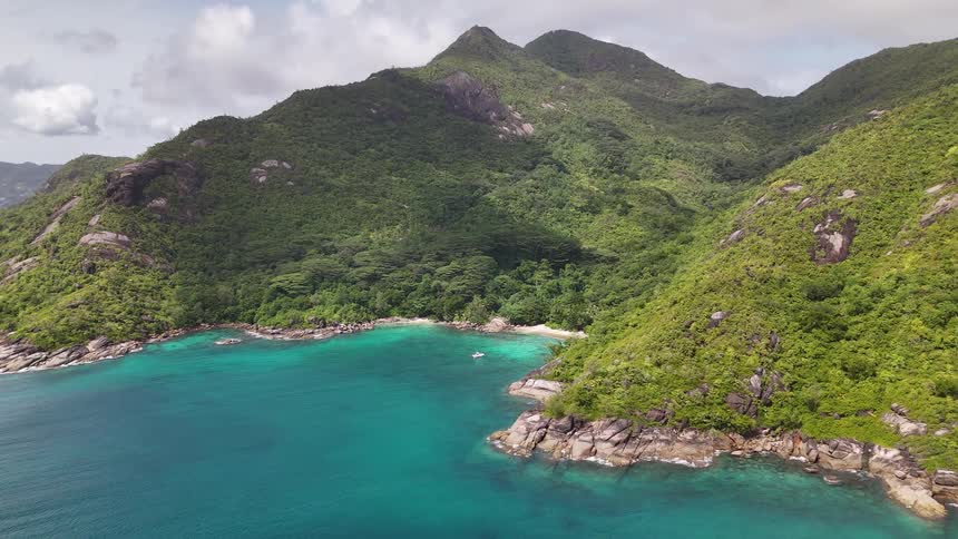 A mountain island is surrounded by ocean water with the mountain covered in green vegetation