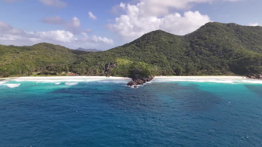A beautiful aerial shot slowly pulls back from a tropical coastline revealing white sand beaches turquoise water and vast lush green hills