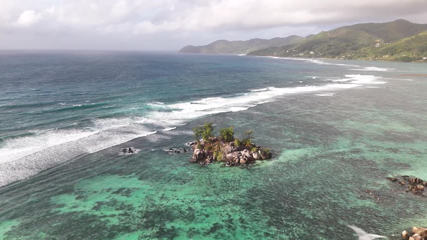 Flying up and away from a small tropical islet the camera reveals a stunning coastline as seagulls fly through the scene