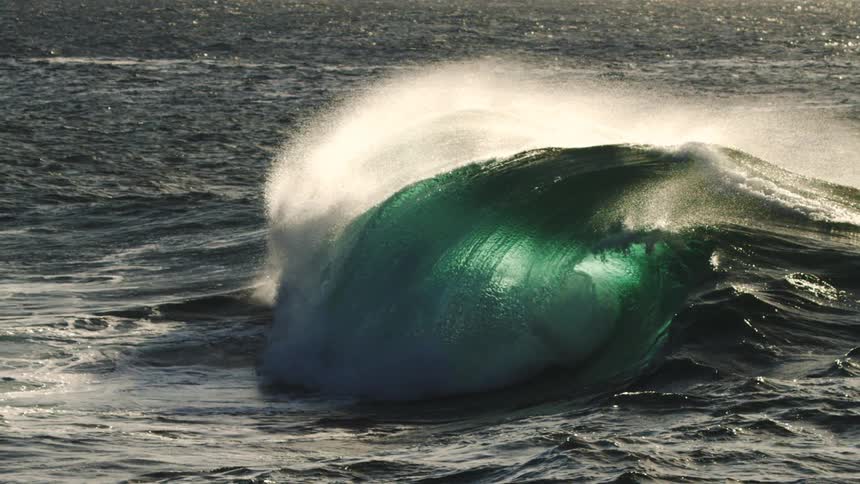 A powerful ocean wave crashes with intense spray under bright daylight