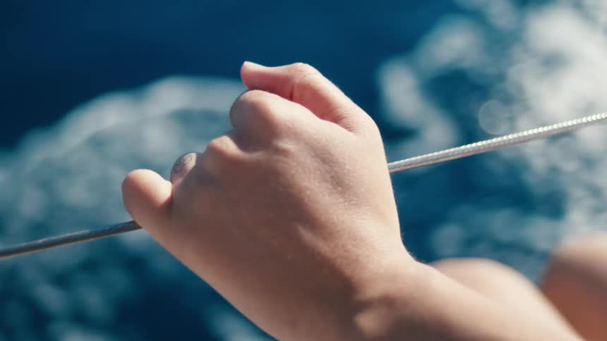 A closeup of a persons hands holding onto a rope or cable with blurry blue water visible in the background suggesting movement on water the hands appear to be firmly gripping the line