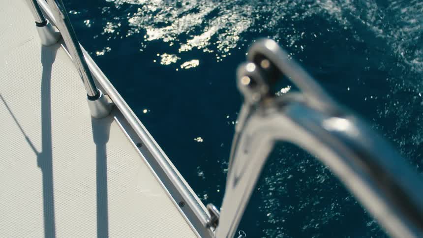 The feet of a man jumping off a boat above sunlit blue ocean water
