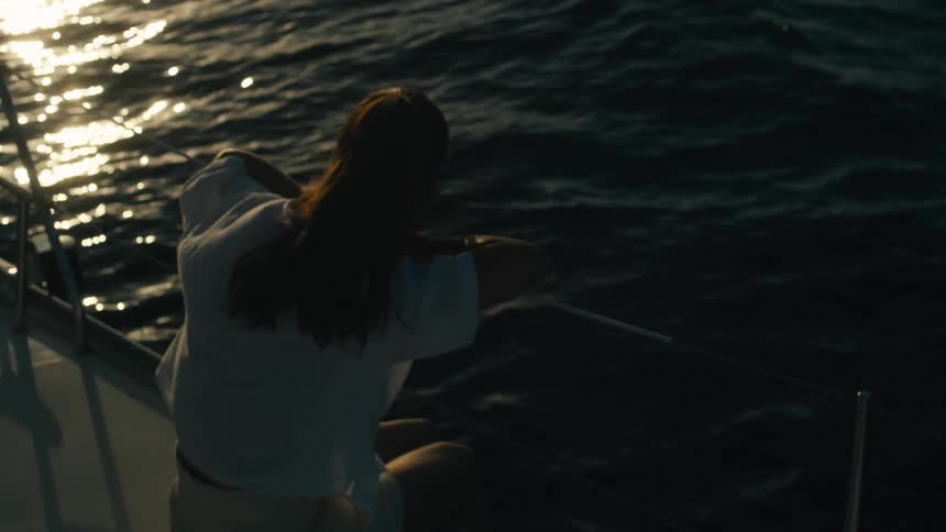 A woman sits quietly at the edge of a boat looking out over the dark waters