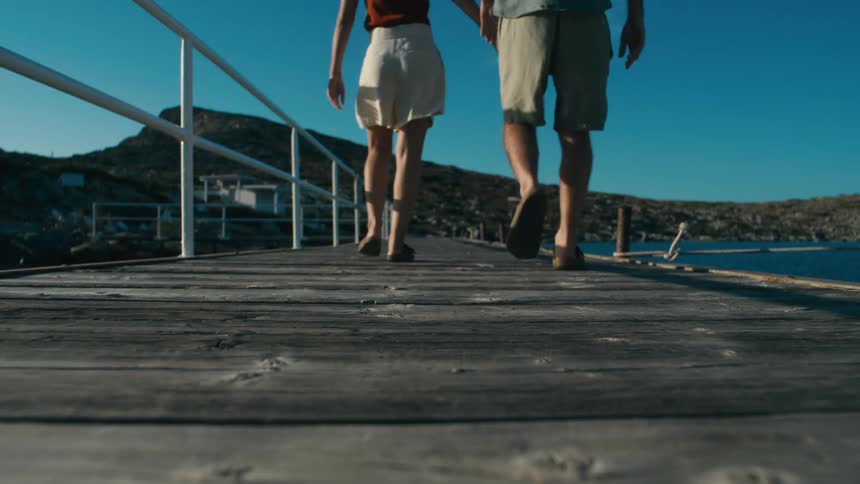 Couple holding hands and walking along a wooden pier