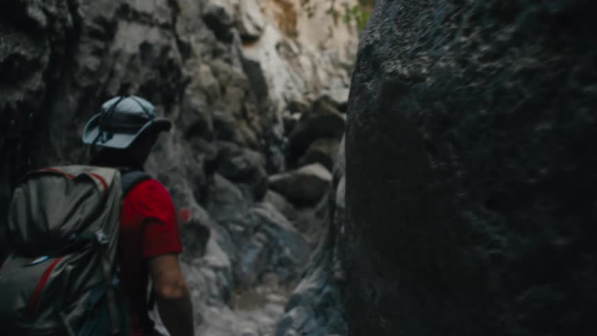 A hiker with a backpack and sunhat navigates through a tight rocky canyon path
