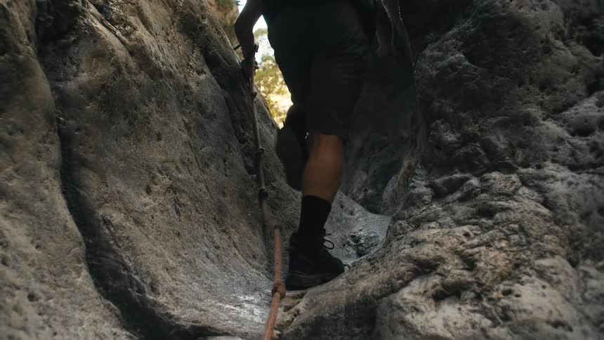 The man is climbing up the rocks as he hikes