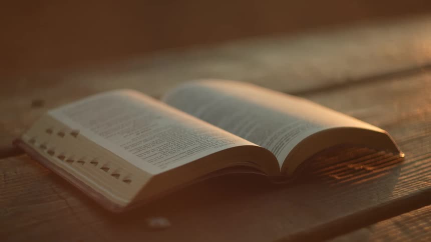 Open bible laying on a wooden table outdoors