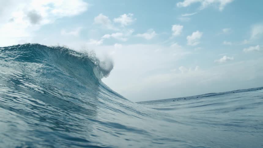 People float in the water as a nearby wave swells and breaks on a cloudy day