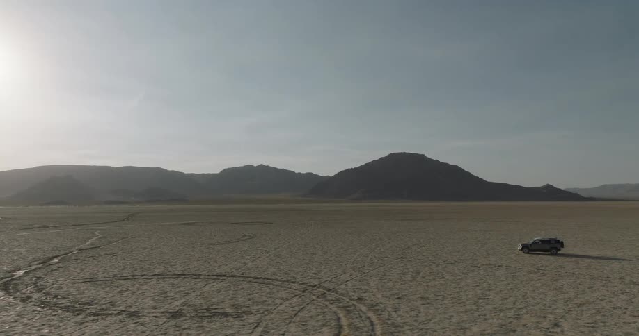 Isolated car traveling through a large area with mountains in the background