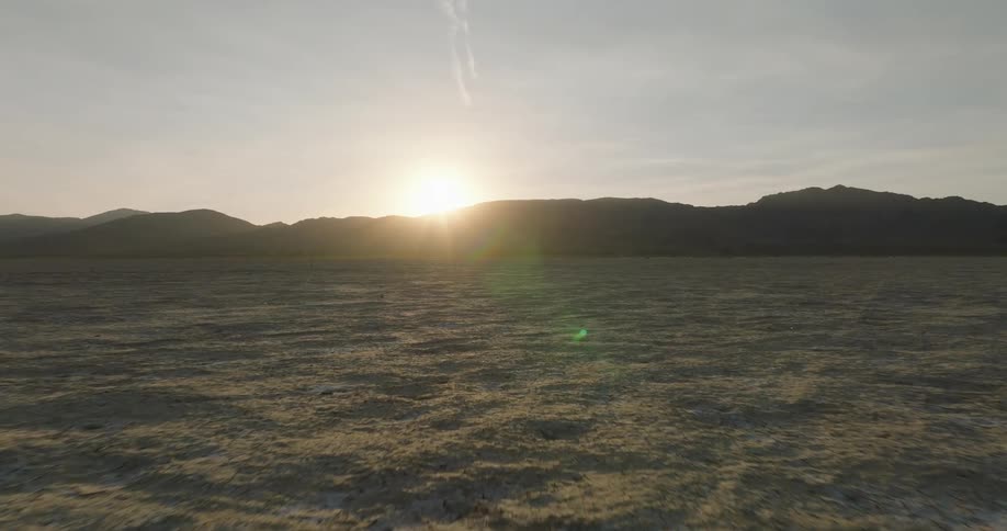 Dry field with silhouettes of mountains on the horizon and the sun