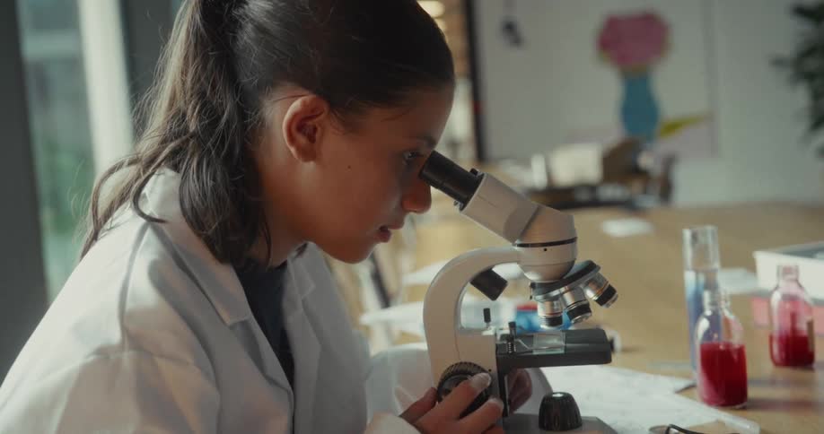 The girl is adjusting the microscope as she uses it