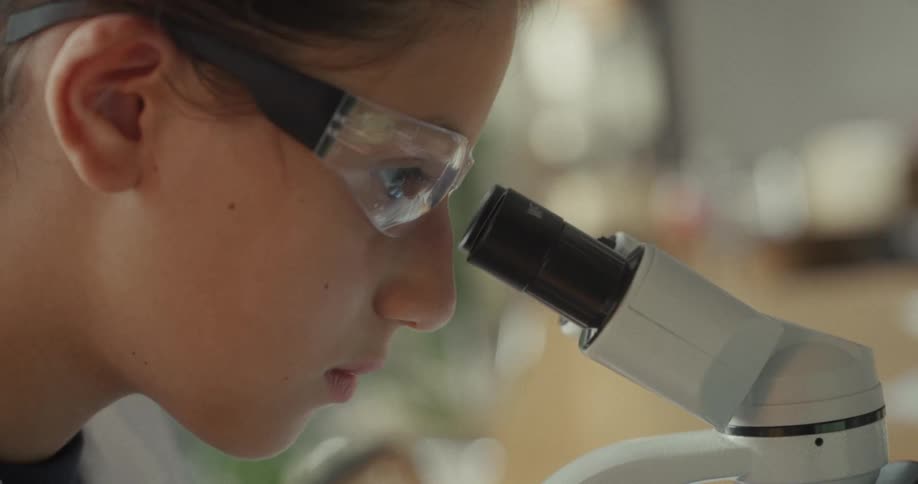 Close up of a young female scientist looking into a microscope lens in a lab during daytime