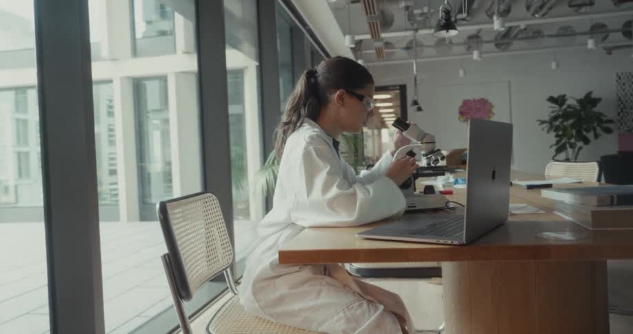 A girl is using a microscope and laptop