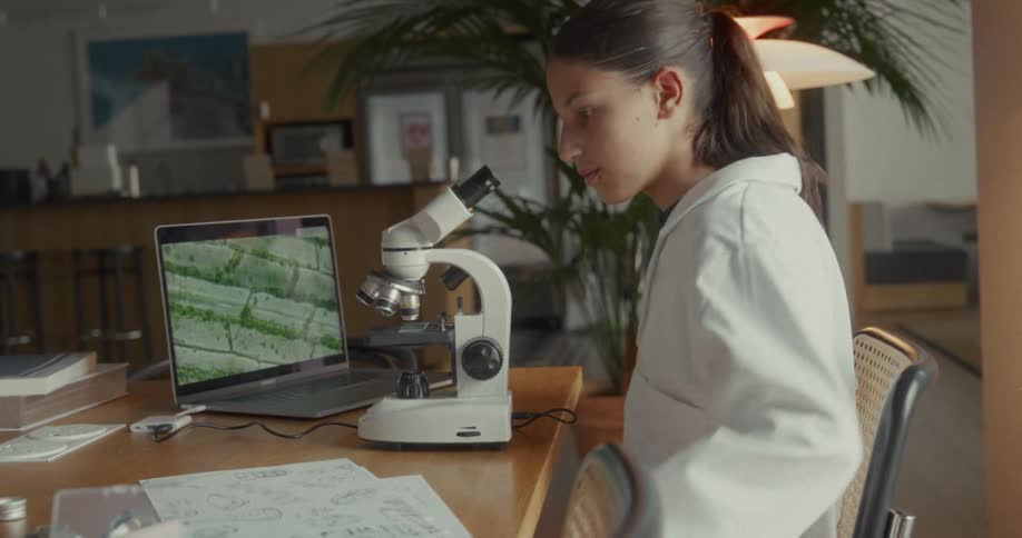 Teenager sitting at table and handling microscope