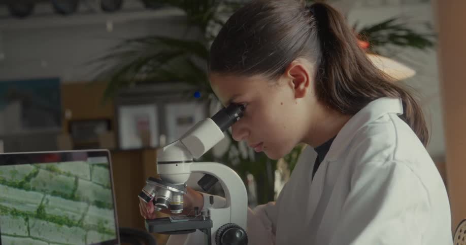 The laptop is showing images of what the girl is viewing in the microscope