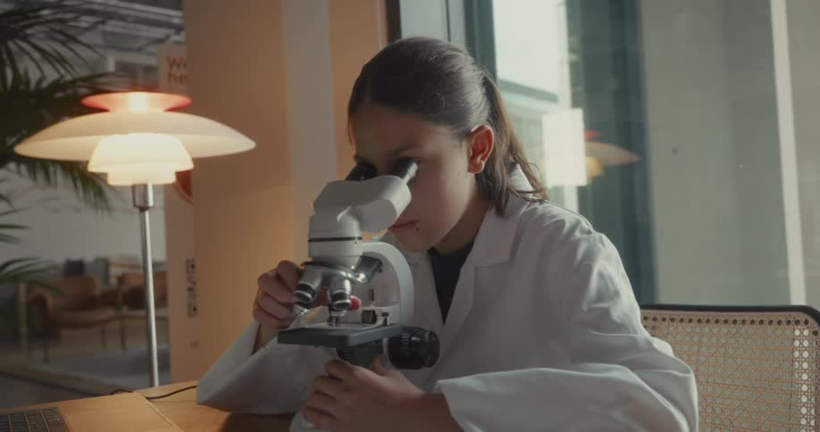 Close up of a female scientist viewing a slide on a microscope at a table in a lab during daytime