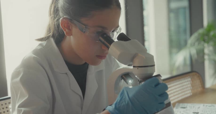 The teenager holds the microscope and views a slide