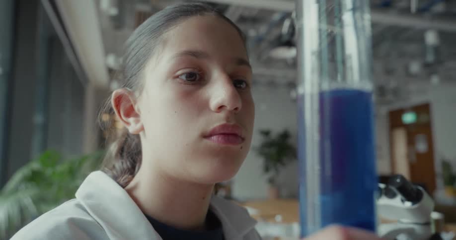 The girl examines blue liquid in the beaker