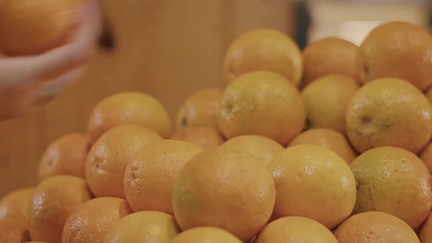 A persons hand reaching into a pile of oranges the hand adorned with a ring and a smartwatch selects an orange and then moves out of the frame the oranges are brightly colored and appear to be in good condition