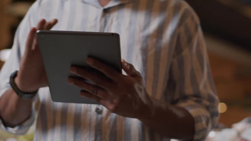 A person in a striped shirt interacts with a tablet while standing beside a produce display in a grocery store