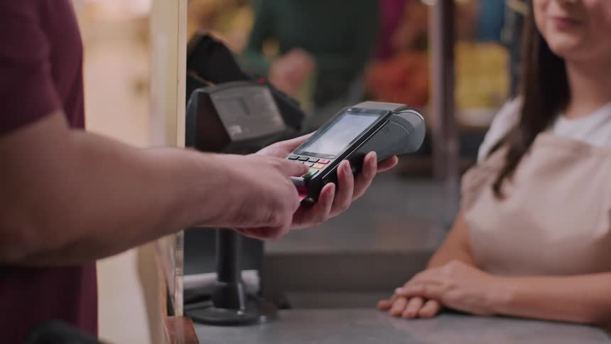 The video shows a customer at a checkout counter attempting to pay with a red card an employee wearing an apron is holding the payment terminal and it appears the card is being inserted into the terminal for a transaction