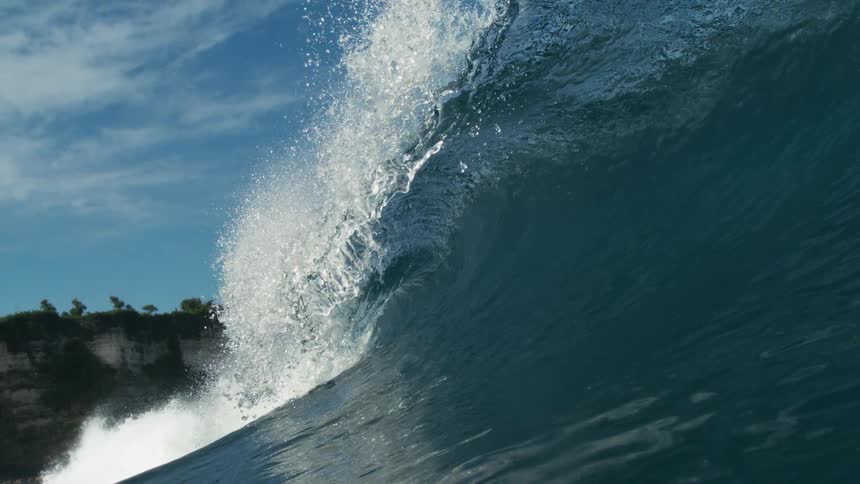 A huge ocean wave crashes hard against a cliff