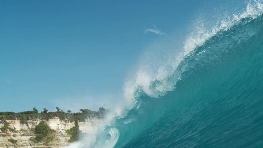 Large blue wave moves past the cliff