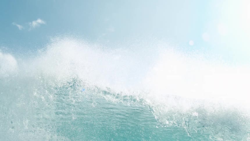A clear blue wave rises under a bright sunny sky