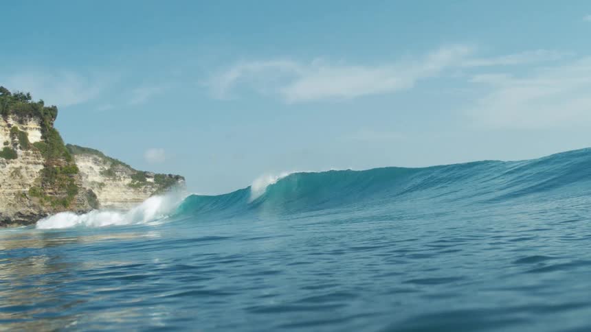 Ocean waves roll toward a rocky coastal cliff under a clear blue sky