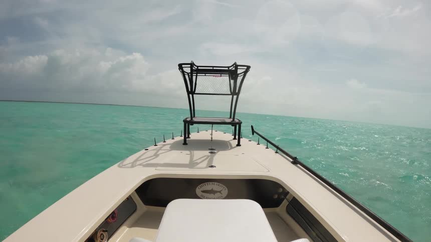 A boat moving through calm clear turquoise water under a partially cloudy sky the camera is positioned at the front of the boat offering a view over the bow as it glides across the serene ocean surface the water is so clear
