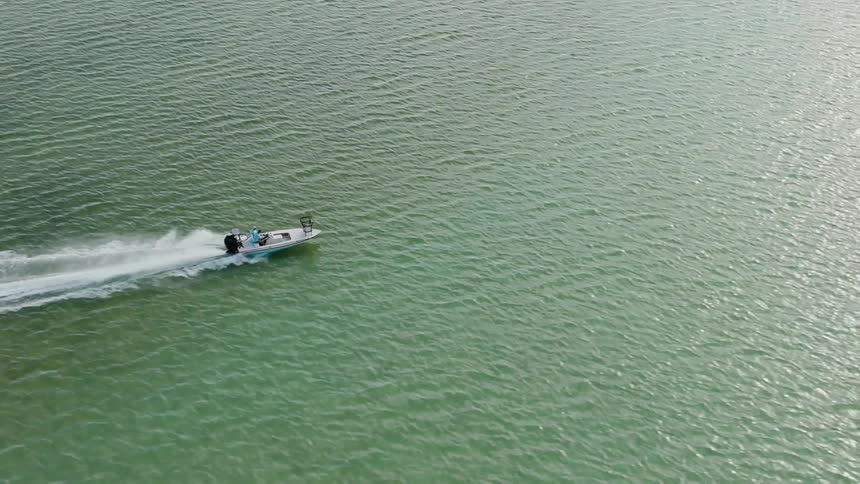 A small speedboat moves quickly across a calm river near a forested shoreline