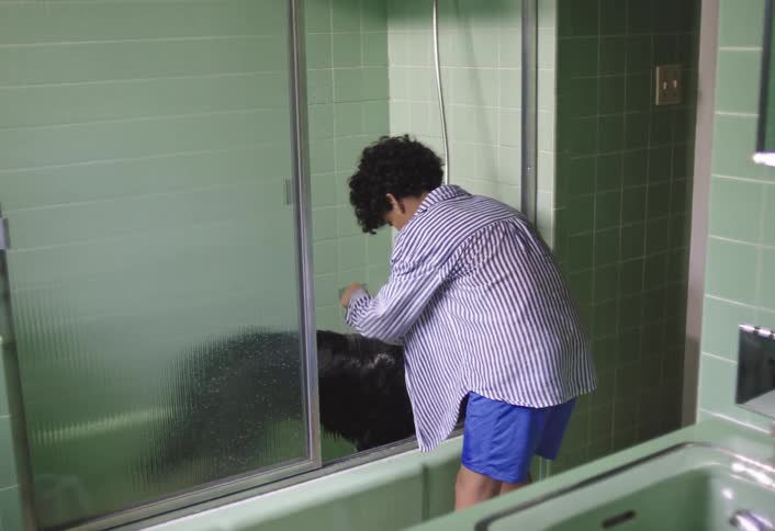 The boy is spraying his dog with water in he tub