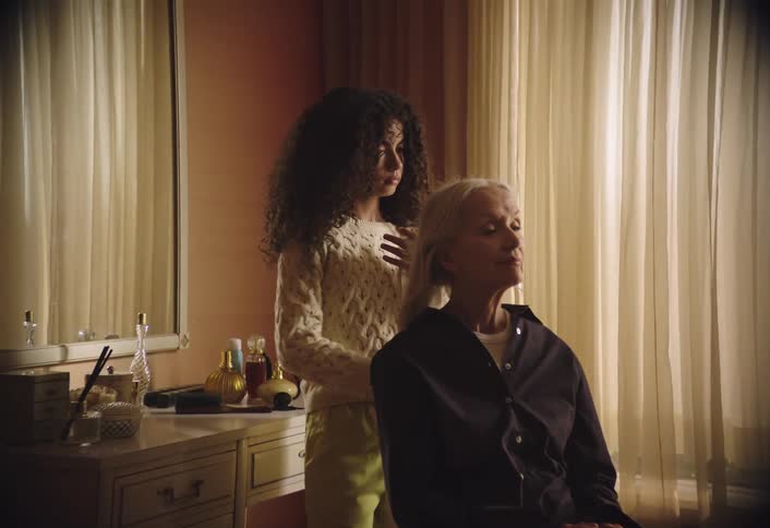 A little girl brushes an elderly womans long hair in a bedroom