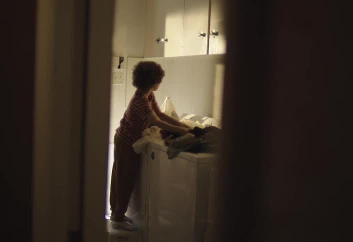 A little boy takes laundry out of the dryer folds it and smells it