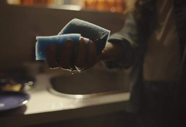 A girl by the sink squeezes water out of a sponge