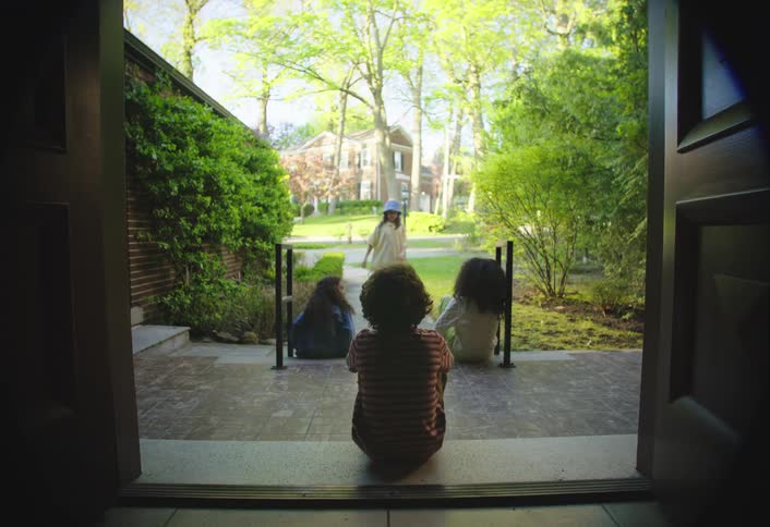 Three children sitting watching one dancing in the backyard