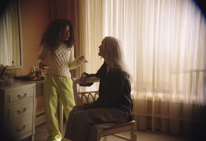 Curlyhaired child standing and talking to a woman sitting in the chair next to her