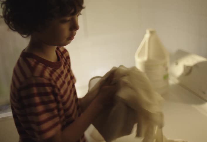 A child is in the laundry room picking clothes out of the laundry machine